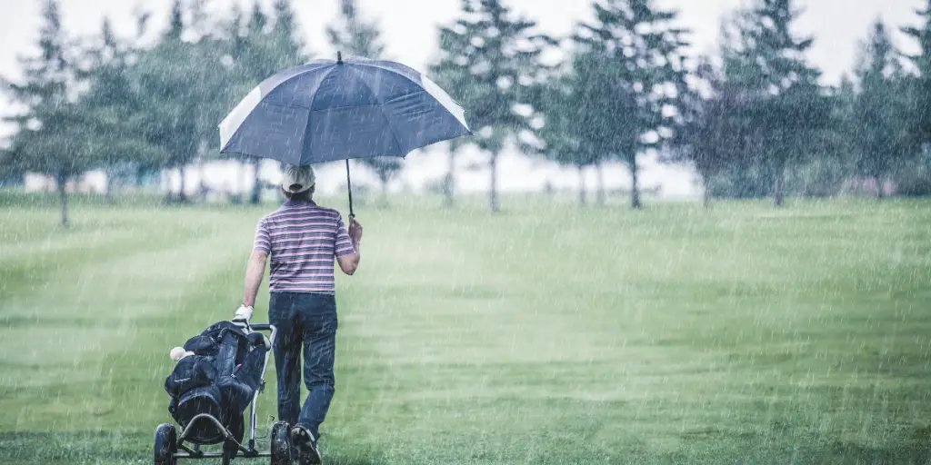 man walking on golf course with pull cart and umbrella